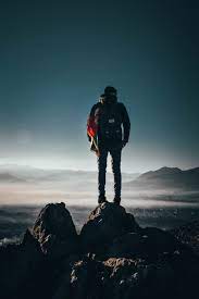 man carrying backpack standing on rock
