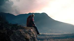 boy sitting alone on high mountain rock