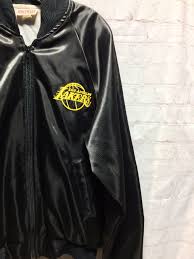 The jacket has a v neckline, elbow length sleaves with turn ups, a four button front opening and pockets on either side. Los Angeles Lakers Satin Acetate Zip Up Bomber Jacket Embroidered Front And Back Logos Boardwalk Vintage