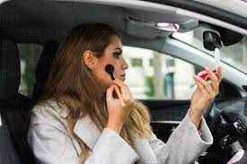 young woman puts on makeup inside a car