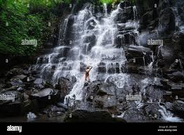 Amazing woman enjoying under stream of big and beautiful cascade waterfall.  Girl with slim fit body and long black hair. Kanto Lampo in Ubud area Stock  Photo - Alamy