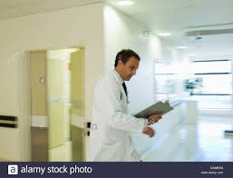 Doctor Reading Medical Chart In Hospital Hallway Stock Photo