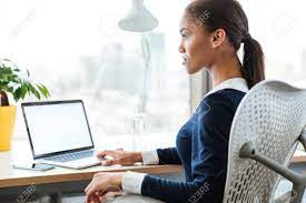 ノート パソコンを窓の近くのテーブルに座っているドレスを着たアフロ ビジネス女性。横から見た図の写真素材・画像素材 Image 68979046