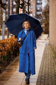 Concetto di tempo piovoso una donna in un cappotto blu con un ombrello blu  su una strada cittadina donna quaranta anni più | Foto Premium