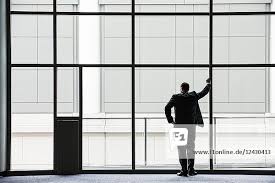 Ein Geschäftsmann in Silhouette, der an einem großen Fenster in der Lobby  eines Kongresszentrums steht.