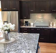 This modern black and white kitchen has a black countertop and white cabinetry that matches the tiled flooring. Favorite Natural Granite Counters To Top Cherry Wood Cabinetry