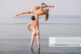 Rear view of nude couple in water jumping in mid air