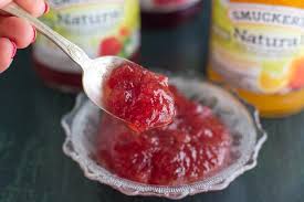 closeup of smucker s natural strawberry fruit spread on silver spoon with jars in background on green