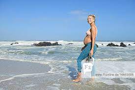 Lächelnde schwangere Frau joggt am Strand