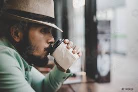 Hipster man drinking coffee from disposable paper cup sitting at - stock  photo | Crushpixel