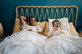 Smiling girlfriend sharing smart phone with boyfriend while lying on bed  stock photo