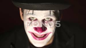 scary clown looks at the camera and