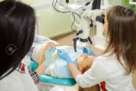 女性歯科医とマスクと手袋を身に着けている歯科医院でアシスタント。美人歯科医歯科用ツール顕微鏡による歯の治療の準備を保持しています。  の写真素材・画像素材. Image 70540951.