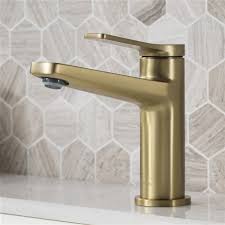 Kohler brushed gold faucet is fixed to a honed marble top beneath a white and gold mirror hung from a white and gray wallpapered wall. Kraus Indy Brushed Gold Bathroom Sink Faucet And Pop Up Drain Rona